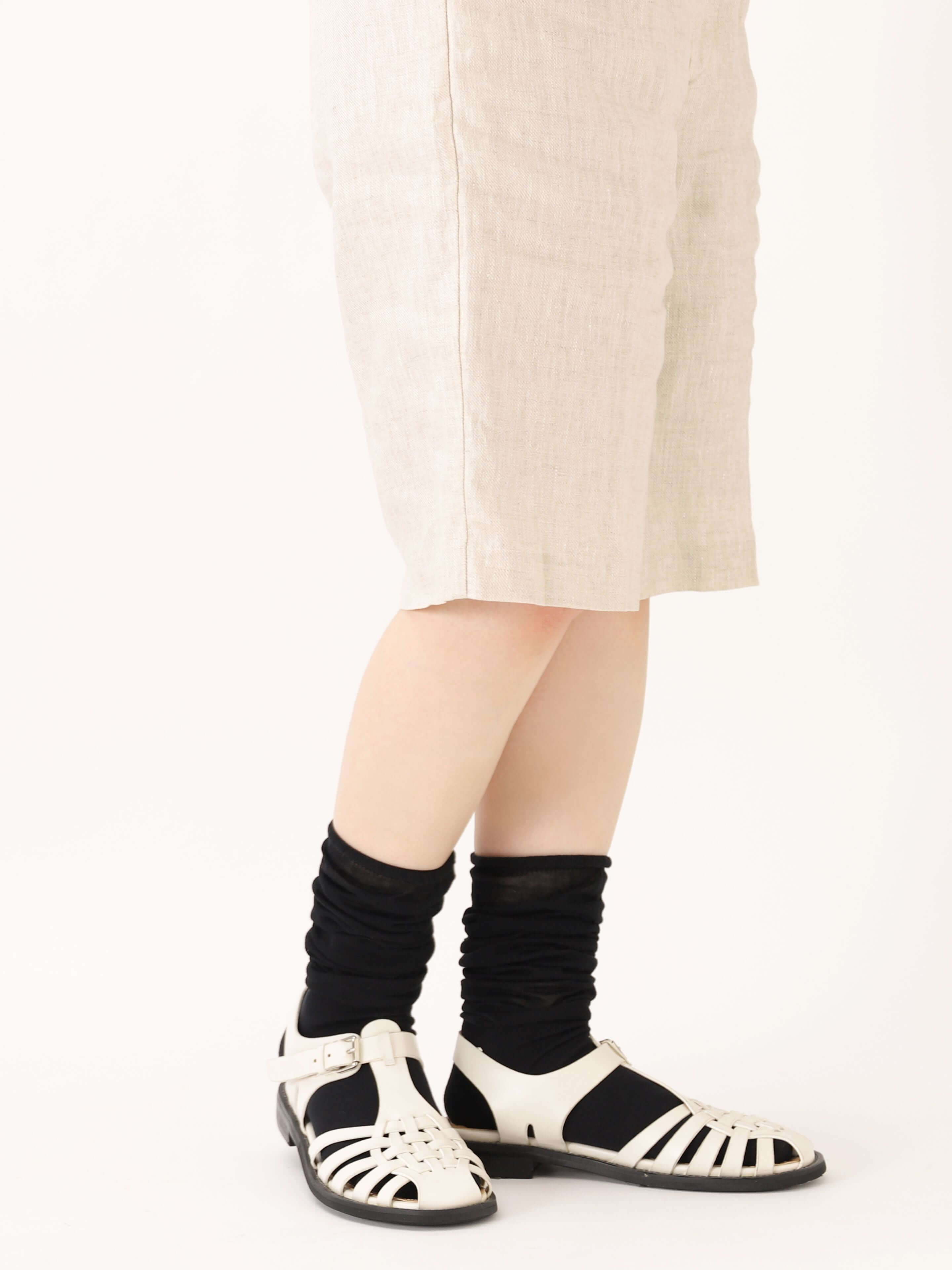 Tabio. Loose-style Light Knee High Socks worn slightly loose with white sandals, showcasing delicate black cotton fabric.