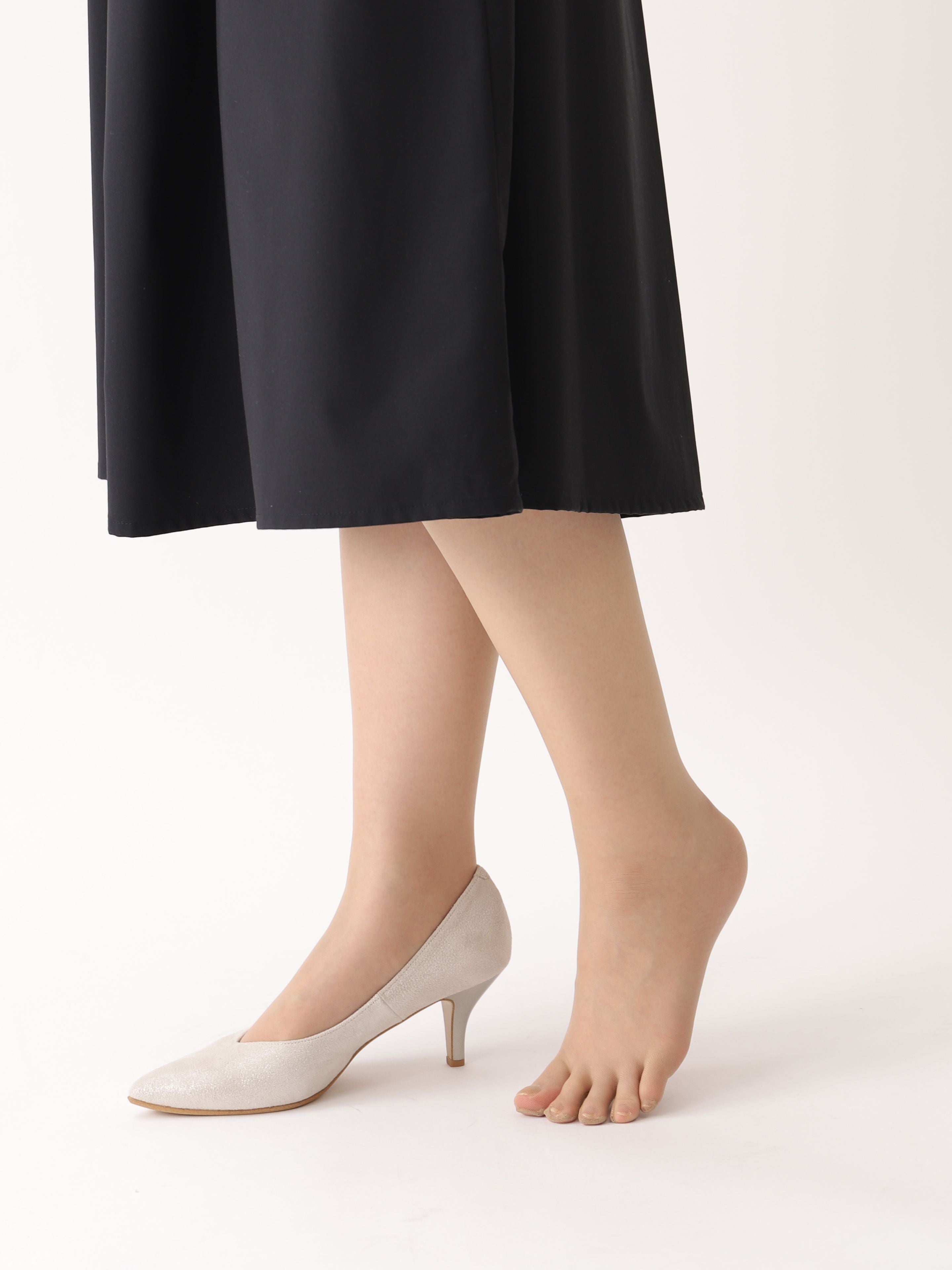 Tabio 20D Sheer Tights on-model side view, nude tone legs with black midi skirt, one foot in beige heel, transparent finish.