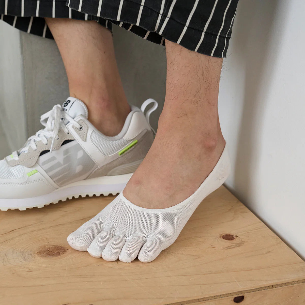 Tabio Lyocell Toe No-Show Socks in white, showcasing toe separation and a low-cut design, worn with sneakers on a wooden.