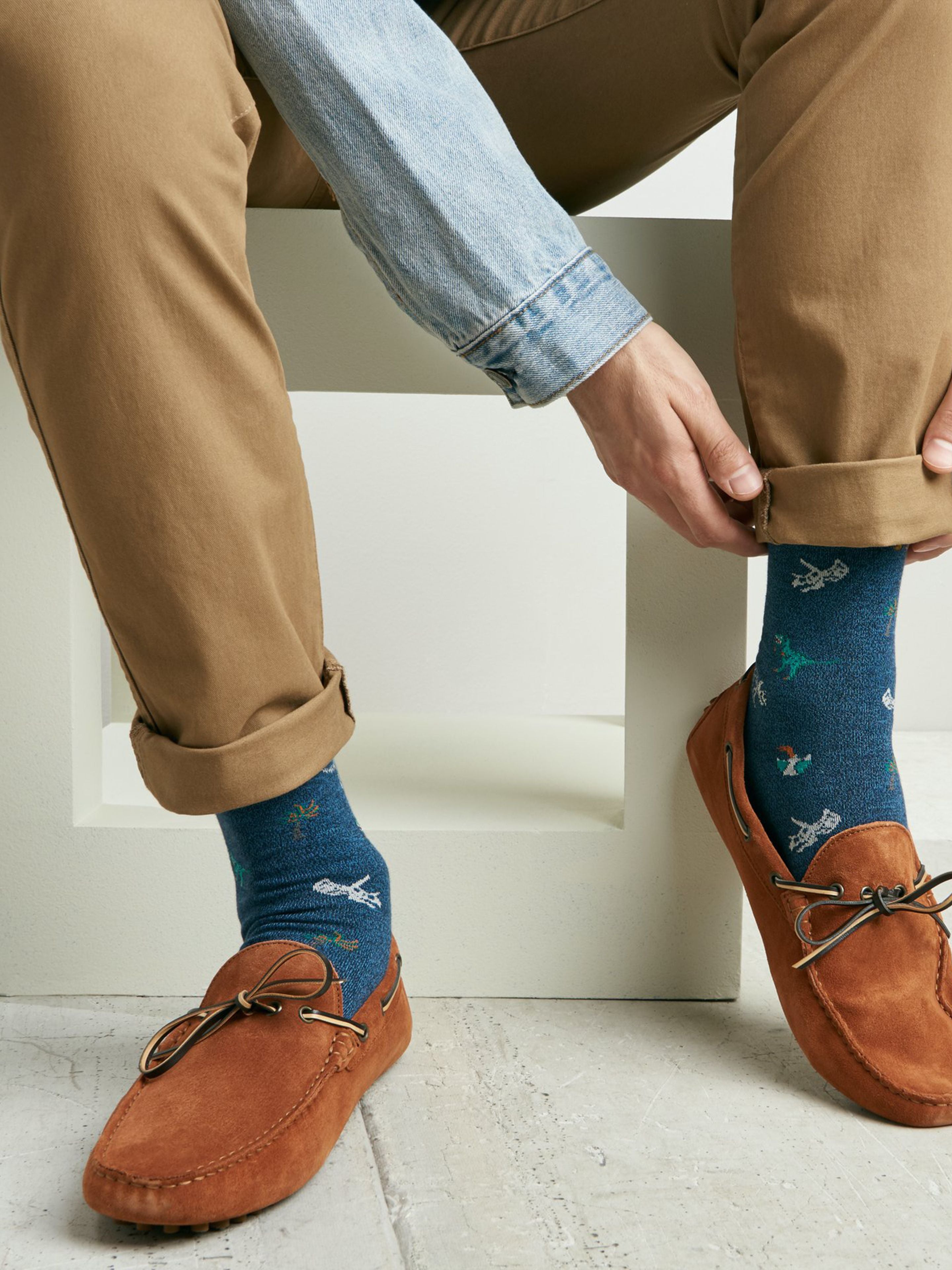 Tabio Dinosaur-Pattern Crew Socks featuring dinosaur motifs, styled with brown loafers and rolled-up khaki pants.