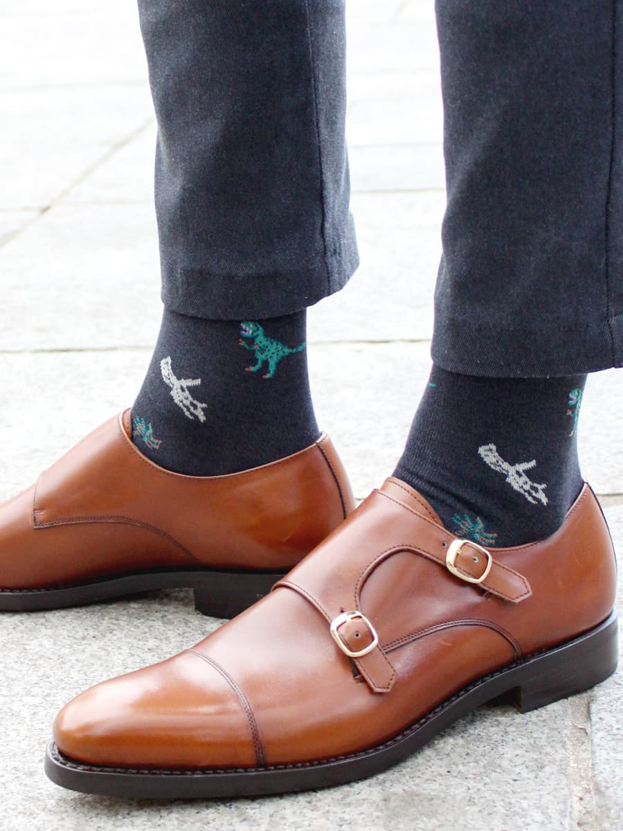 Tabio Dinosaur-Pattern Crew Socks displayed on a model, featuring vibrant dinosaur motifs against a navy background.