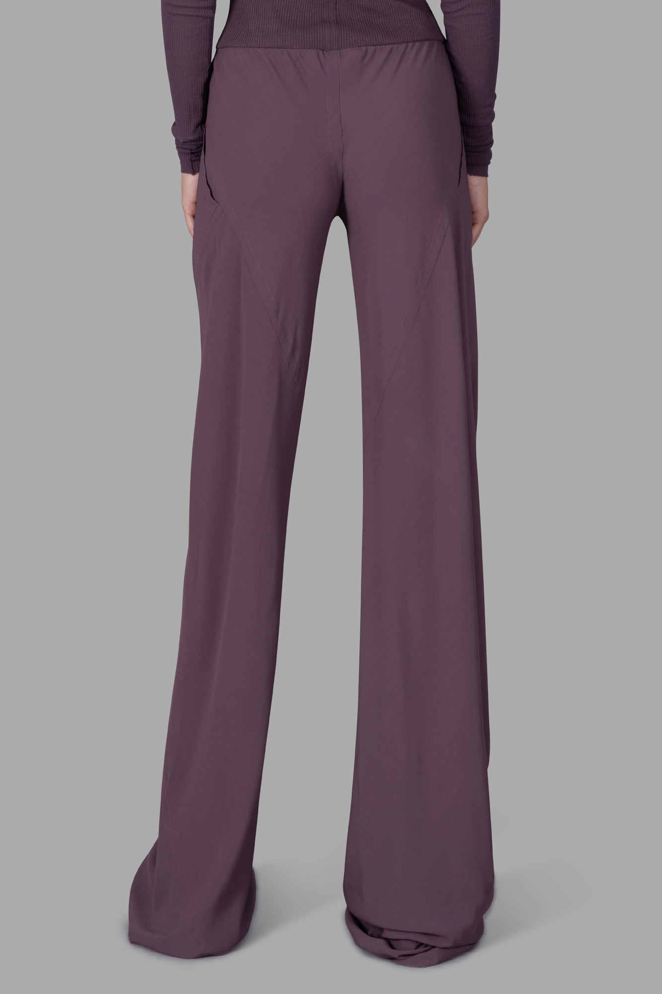 Rick Owens Silk Bias-cut Trousers showcasing a loose fit, ribbed waistband, and raw cut hems in mauve color from the back.