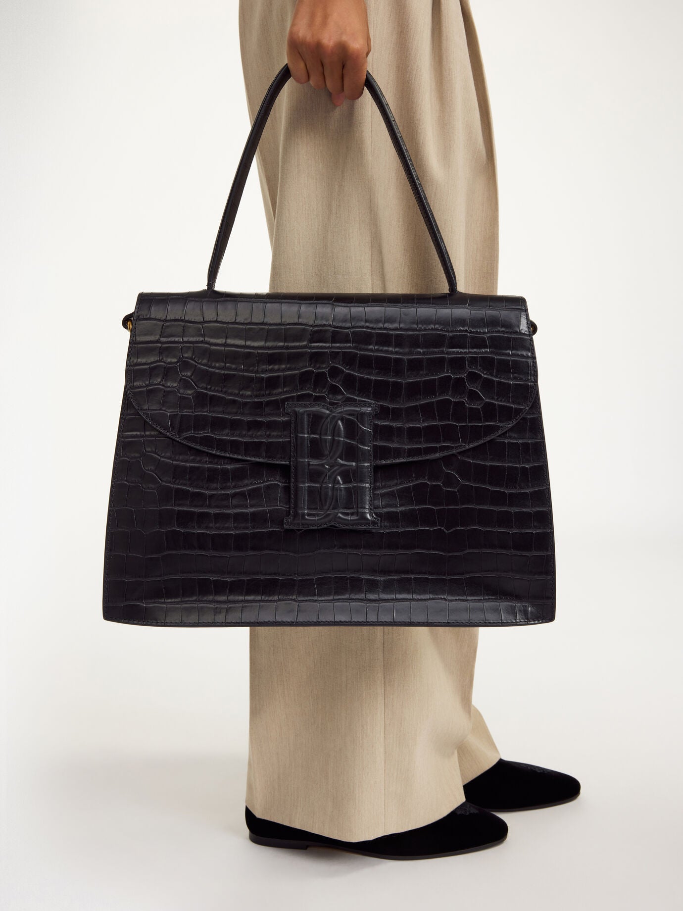 By Malene Birger Ronlas Leather Shoulder Bag held at arm’s length, featuring croco-embossed black leather and top-handle.