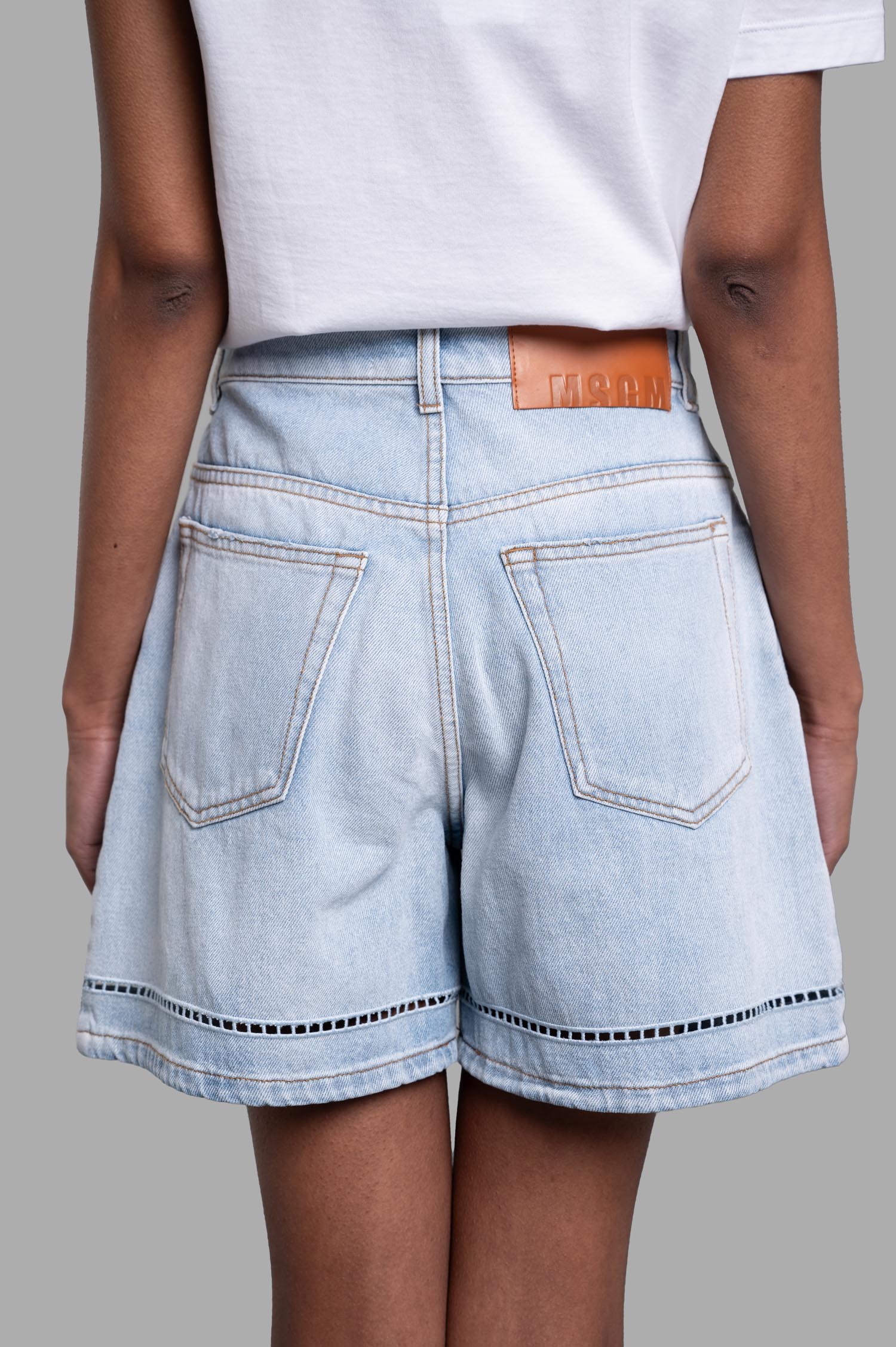 MSGM Perforated Denim Shorts shown from the back, featuring broderie anglaise hem, light blue cotton fabric, and logo.