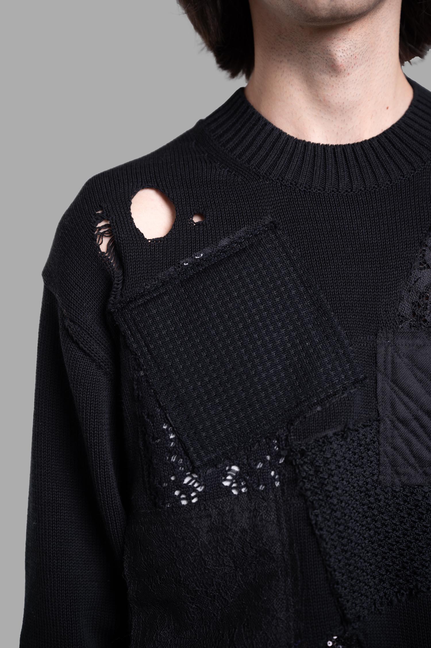 Junya Watanabe Patchwork Sweater featuring black textile details, crew neck, and distressed patches on the front.