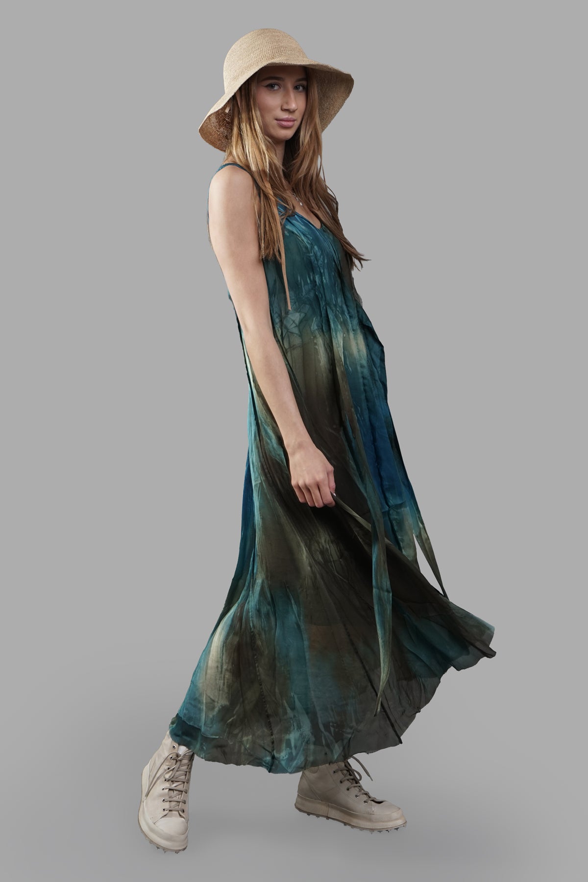 Masnada Abstract-print Dress on-model, side view; flowing sleeveless maxi in teal/green with straw hat and beige boots