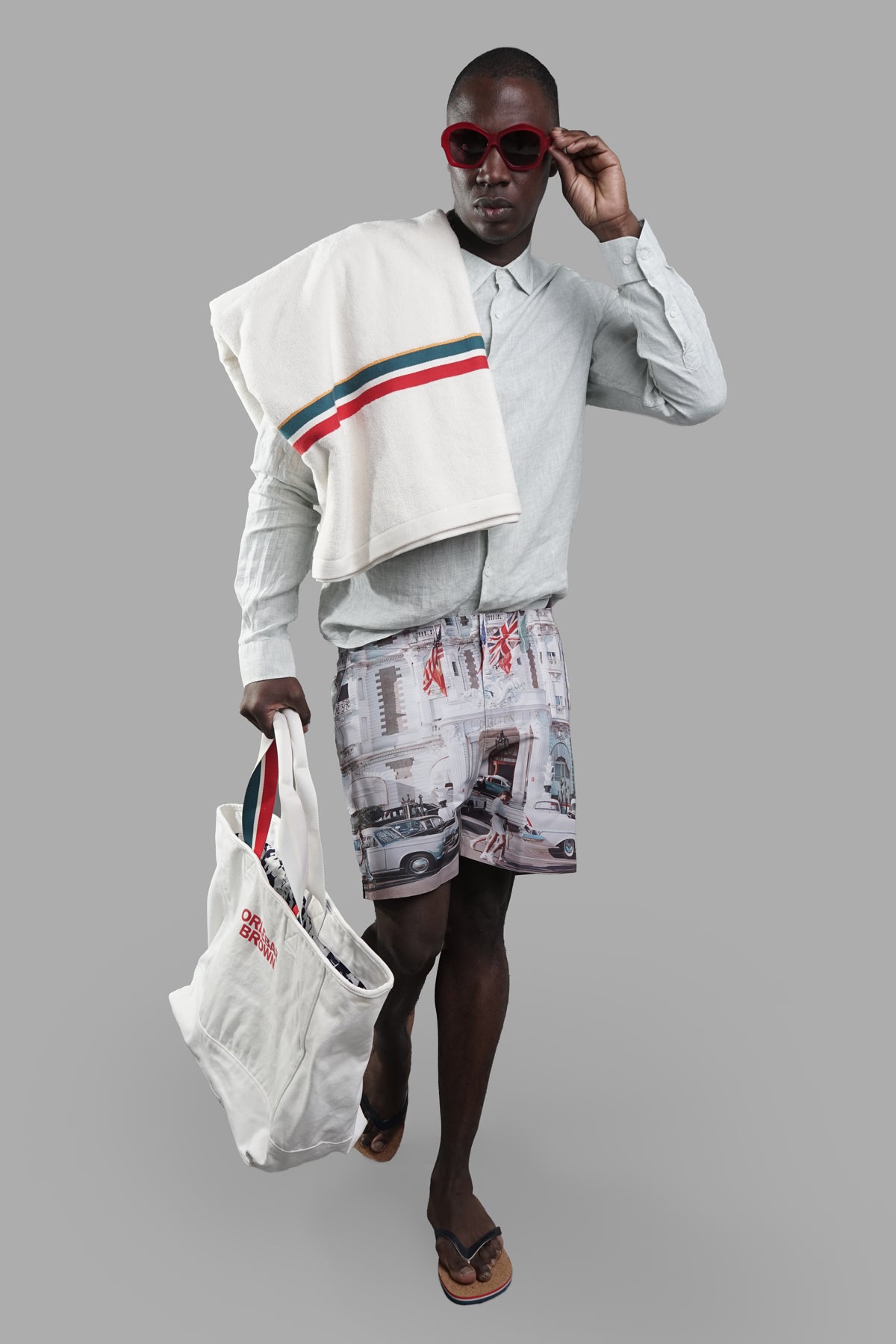 Orlebar Brown Cannes Swim Shorts on model, front view, with white tote and towel draped over shoulder.