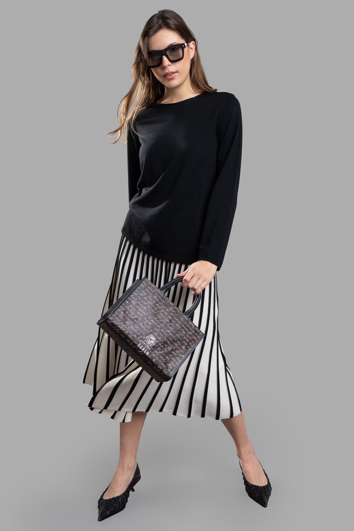 Comme des Garçons Fine-Knit Jumper in black, shown on-model with sunglasses, paired with a striped skirt.