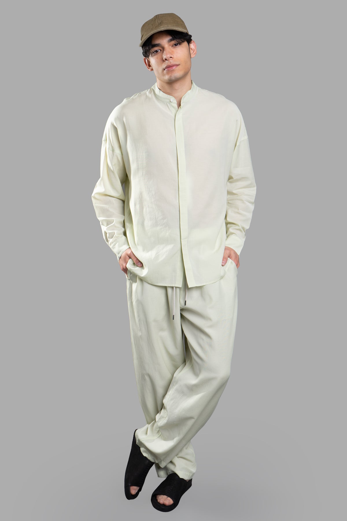 Attachment Collarless Shirt in green, featuring a sleek stand collar and long sleeves, displayed on-model with curved hem.