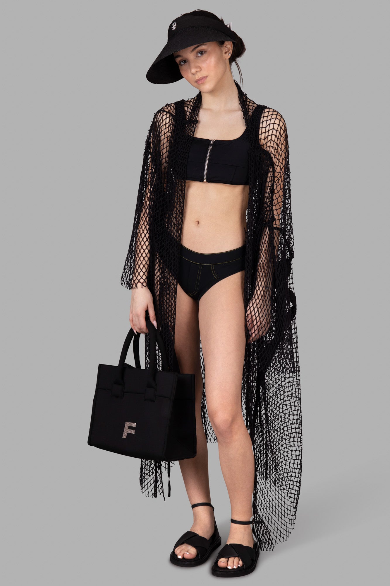 Natasha Zinko Corset-style Bikini Top in black, shown on model with mesh cover-up and visor, featuring zip detail.