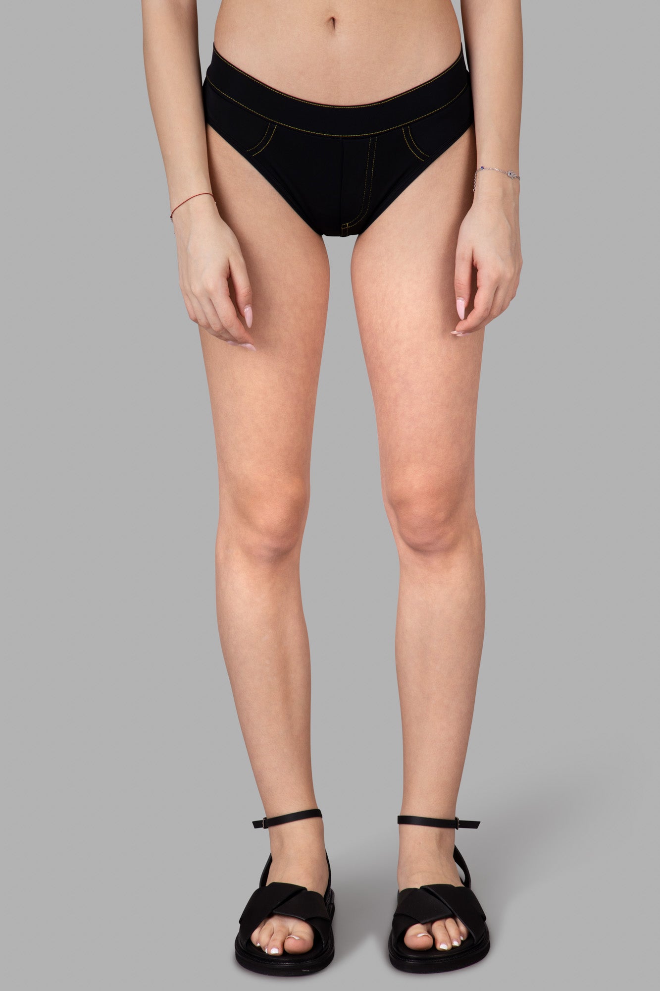 Alt text: Natasha Zinko Black Bikini Bottoms shown on model from the front, featuring yellow stitching and a comfortable fit.