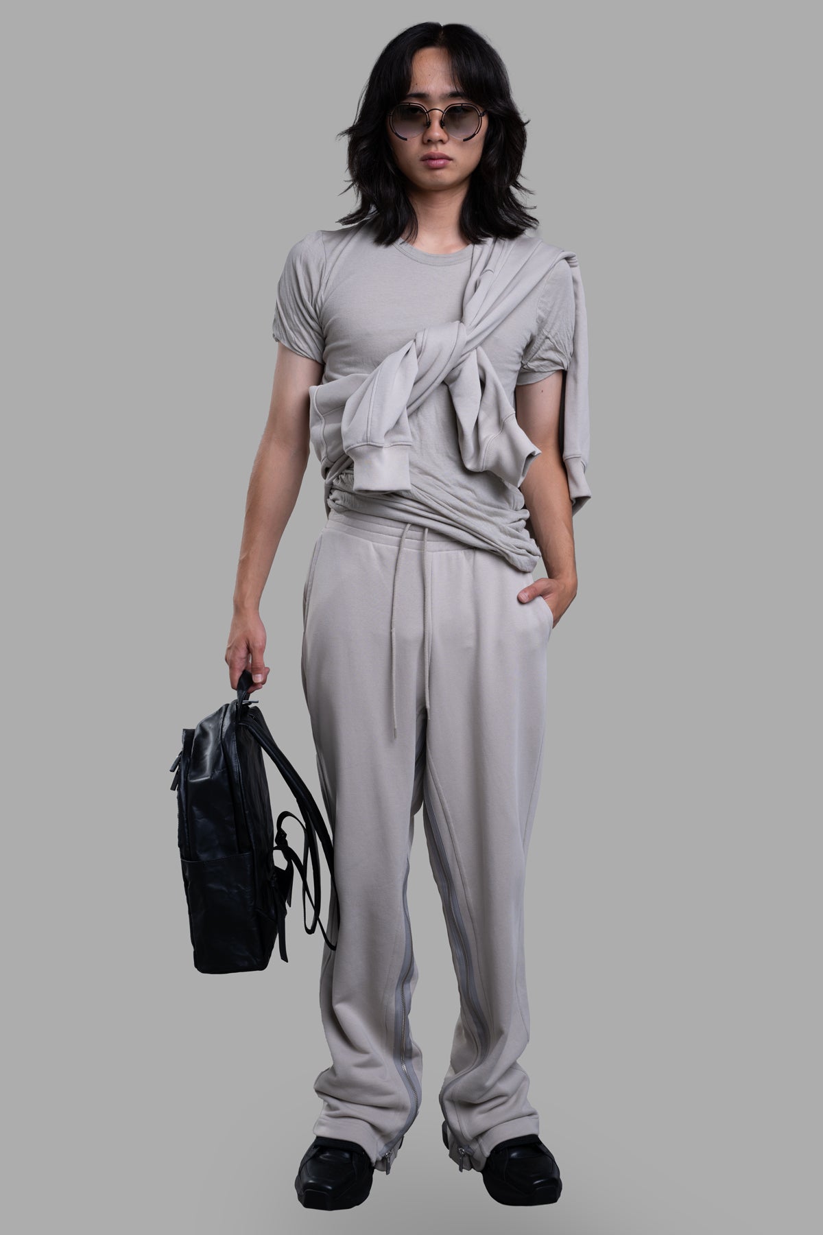 Helmut Lang Gusset Sweatpants in grey, on-model front view, elasticized waist, zippers along legs, holding black bag.