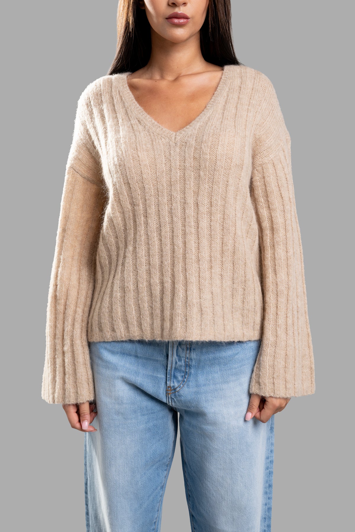 By Malene Birger Cimone Ribbed Sweater in beige, featuring a relaxed V-neck and wide sleeves, styled with jeans.