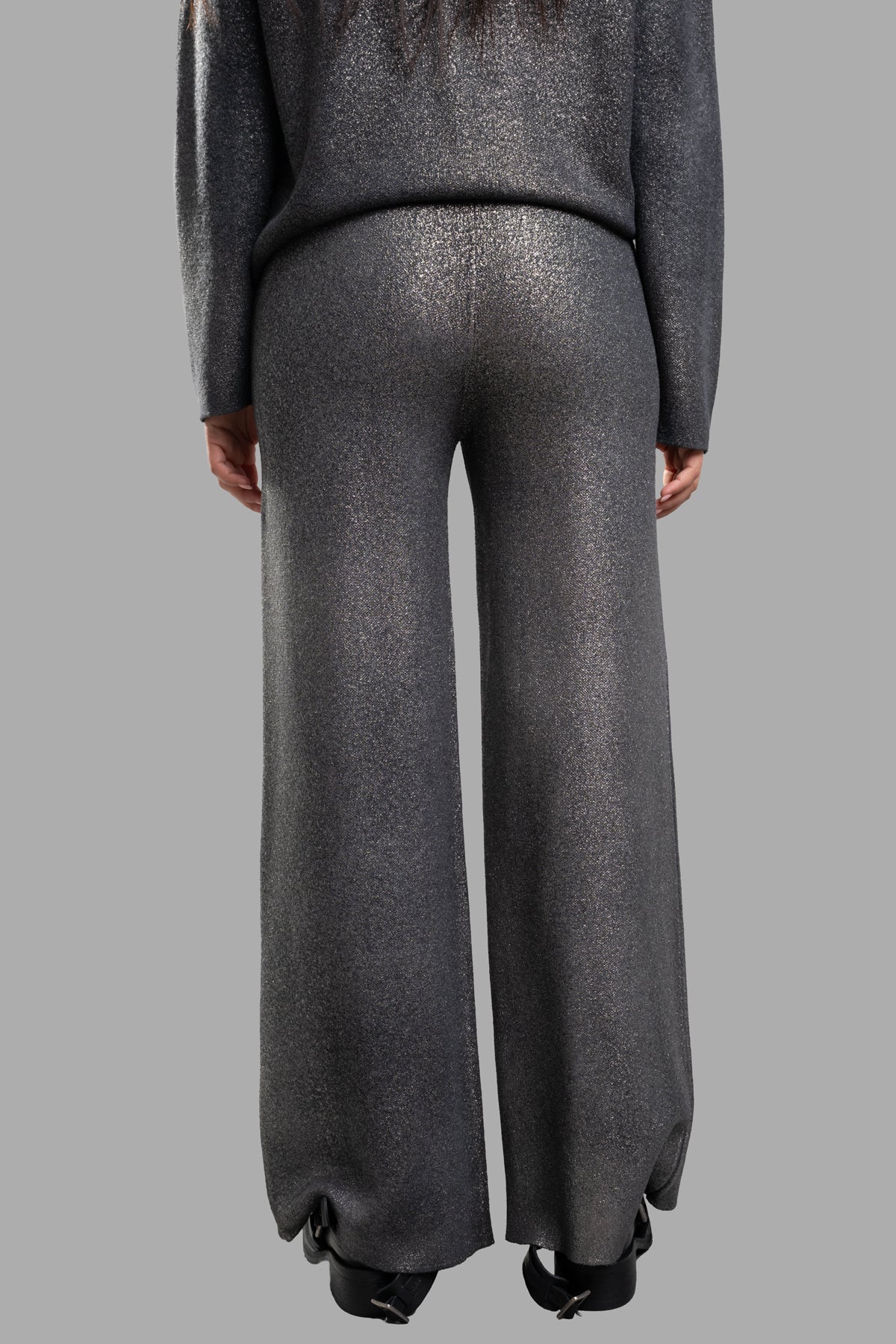 Avant Toi Lamé Knit Pants showcase a high-waisted, wide-leg design with a shimmering grey/gold finish, styled from the back.