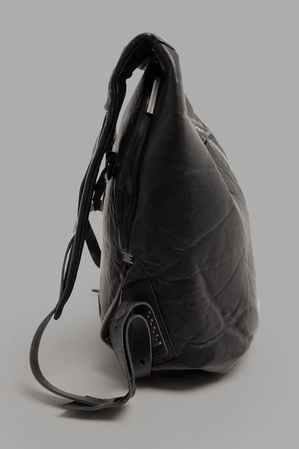 Isaac Sellam Experience unisex leather backpack in black, side view, adjustable strap with riveted tab.