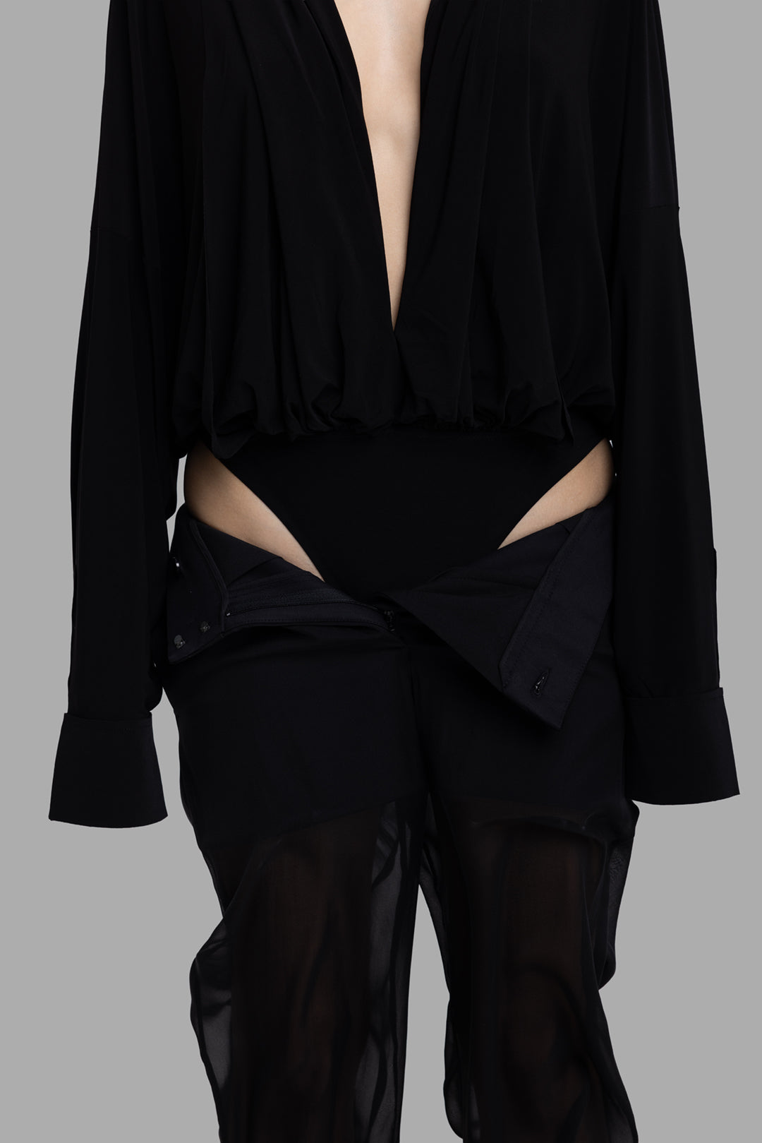 Norma Kamali women’s black hooded bodysuit, close-up showing gathered hem and high-cut brief revealing hips