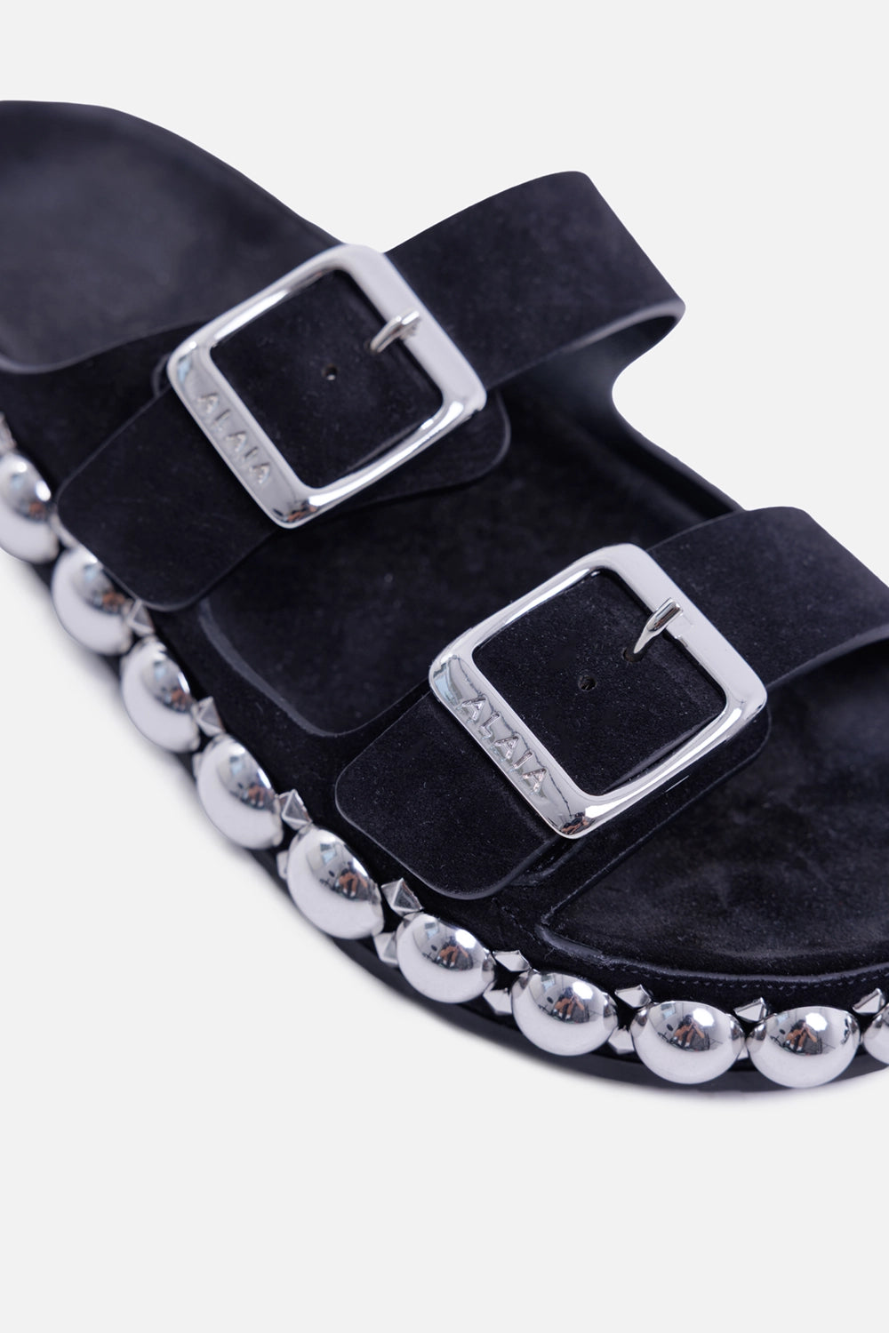 Alaïa women's Bombe suede slides in black, hardware close-up with logo-engraved buckles and polished studs