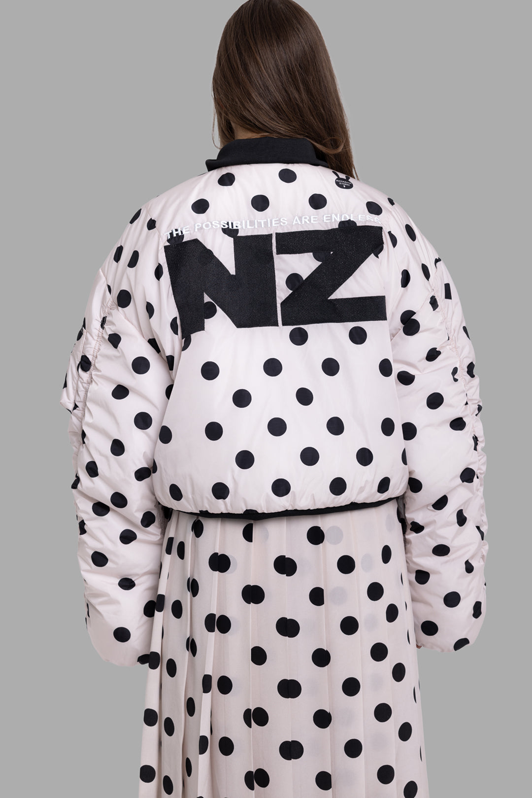 Natasha Zinko women's beige polka dot bomber jacket back view showing large NZ logo appliqué and slogan embroidery.