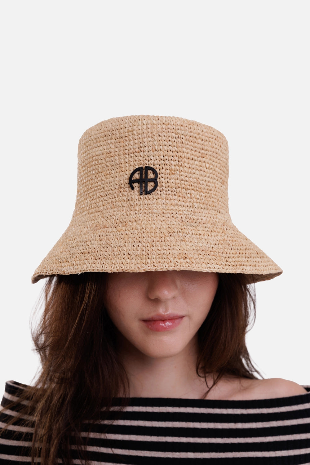Anine Bing women's beige raffia bucket hat, on-model front view with black AB logo and downward-sloping brim
