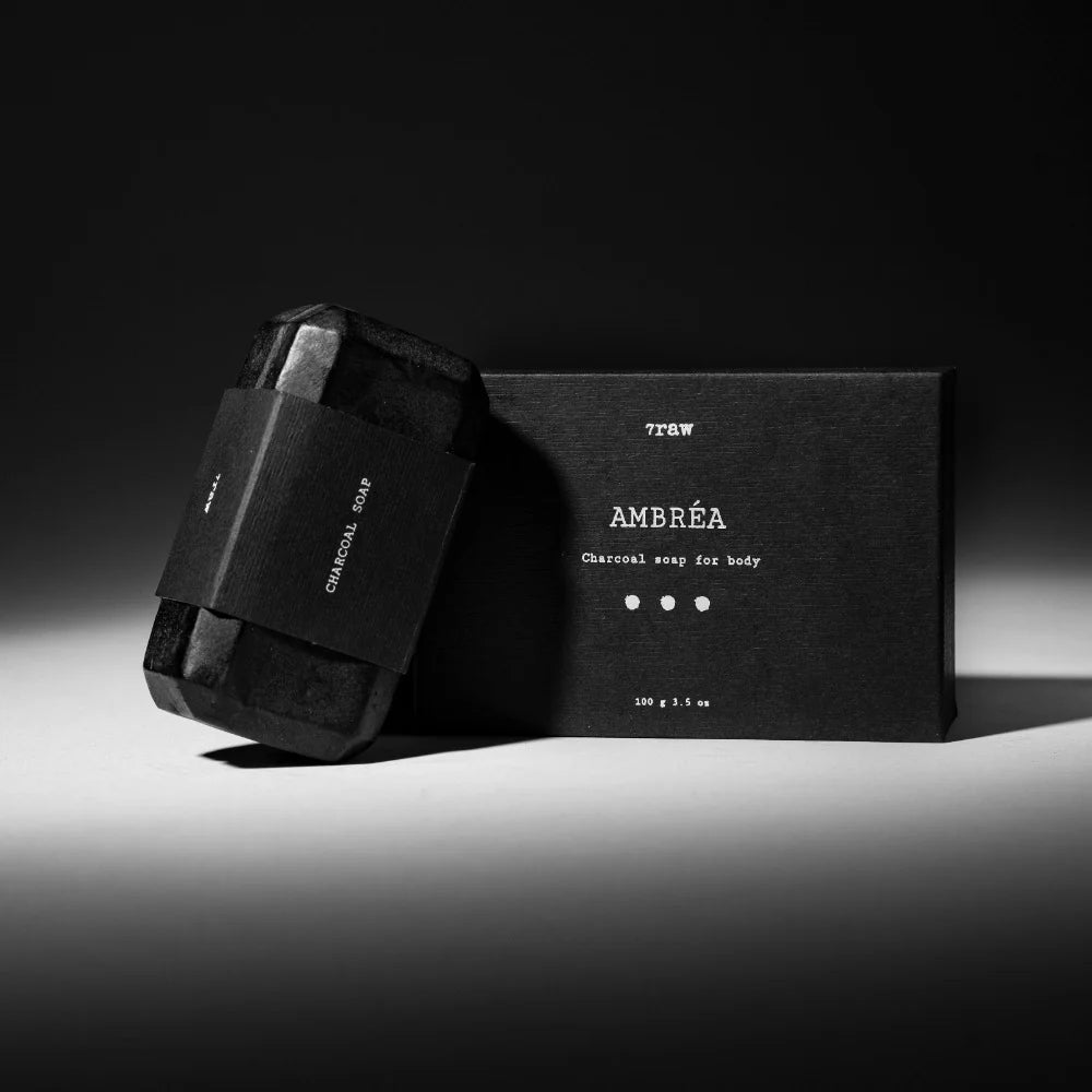 7Raw AMBRÉA Charcoal Soap with front packaging and side view of soap bar on dark background.