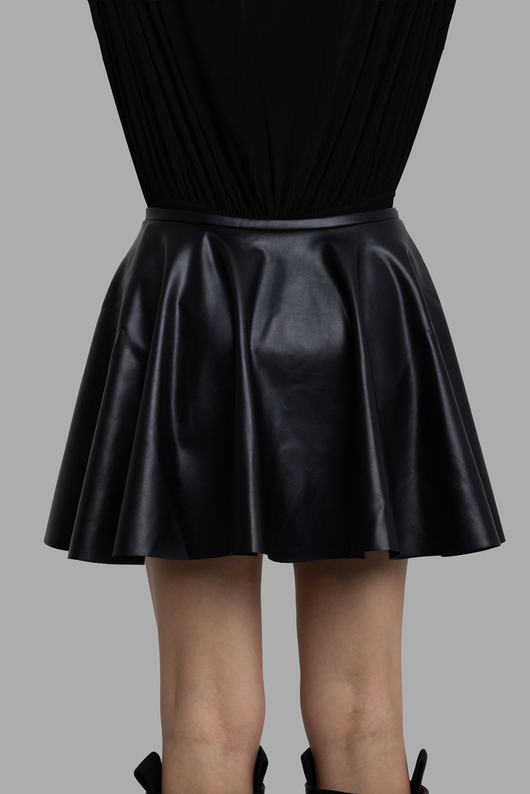 Norma Kamali women's black flared vegan leather mini skirt, back view, clean flare with subtle sheen.