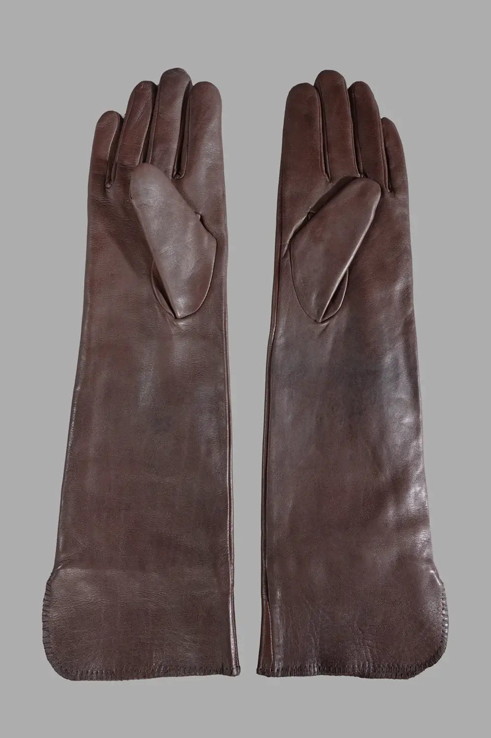 Front close-up of long brown leather gloves showing elongated cuffs and stitched monogram