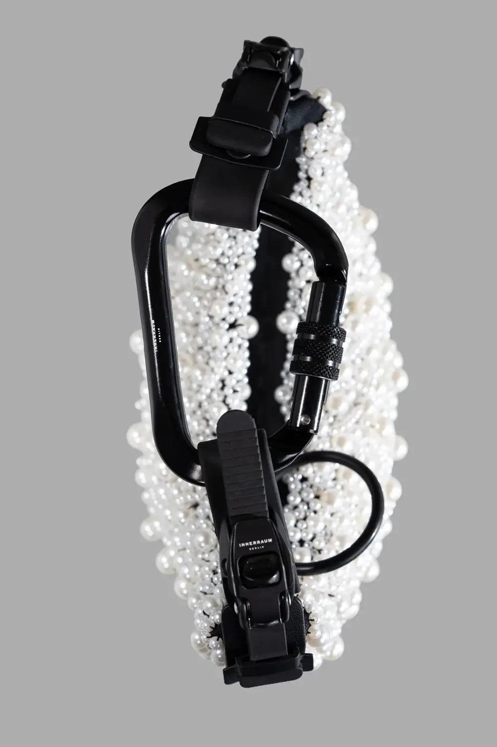 Front close-up of pearl beaded surface with half-moon curve, black matte strap and zip.