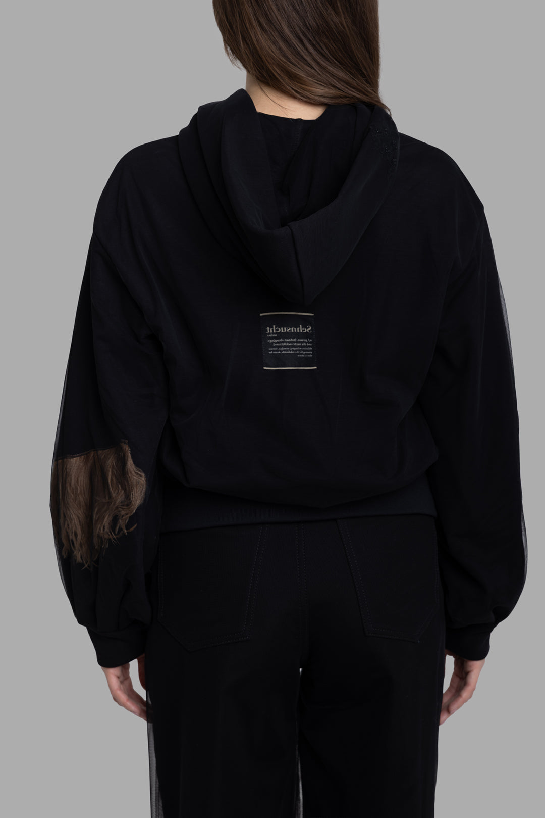 Sehnsucht women's hoodie in black, back view, hood with text patch and feather trim on sleeve.
