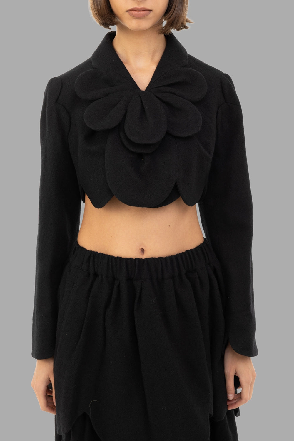 Noir Kei Ninomiya women’s cropped wool jacket in black, front view, 3D petal rosette at collar, scalloped edges
