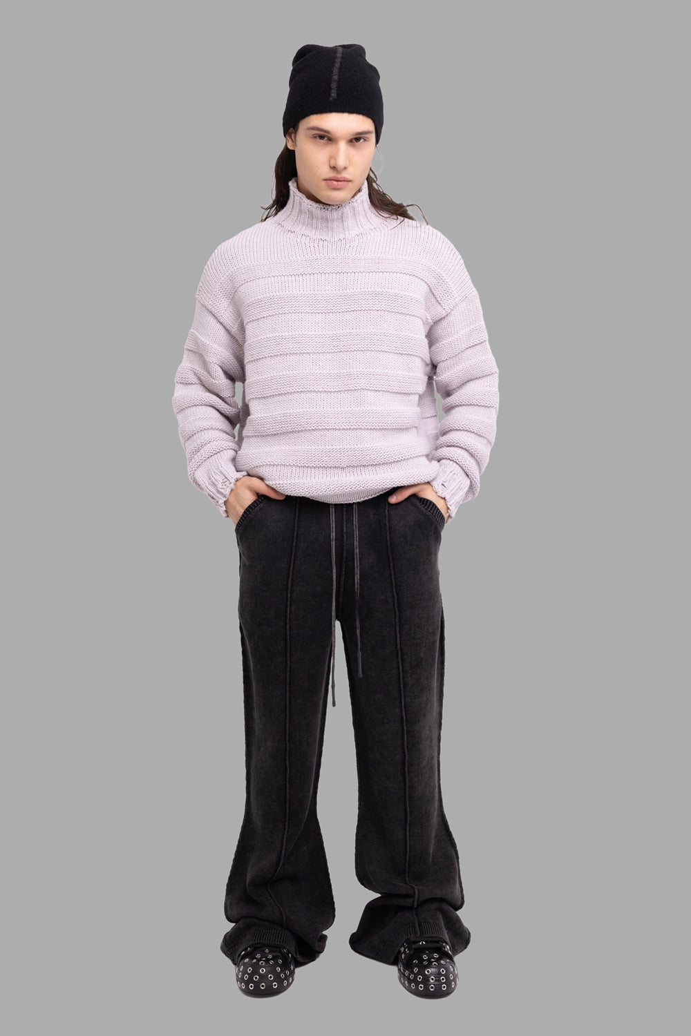 Justin Gall men’s knit pants in black, on-model full length, exposed seams and flared stacked cuffs.