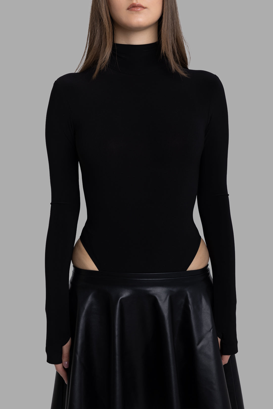 Norma Kamali women's black long sleeve turtleneck bodysuit, close front view showing slim fit and cutout hips.