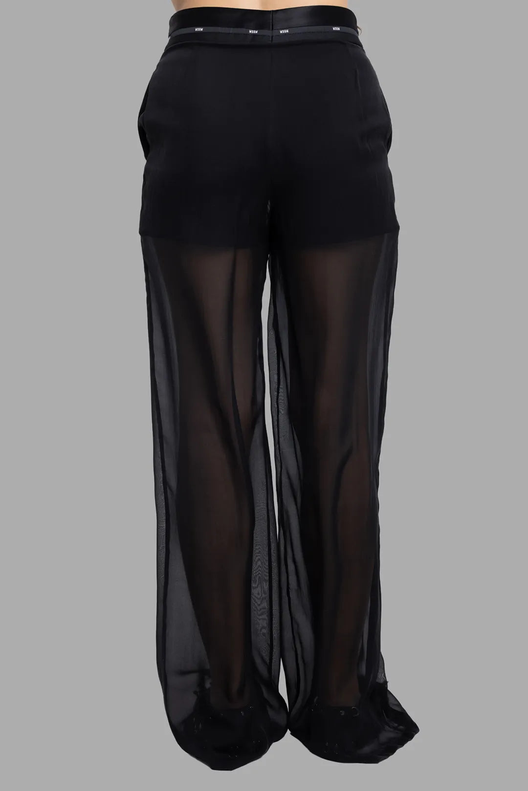 MSGM women's black sheer overlay pants, back view showing logo waistband and flowing transparent legs