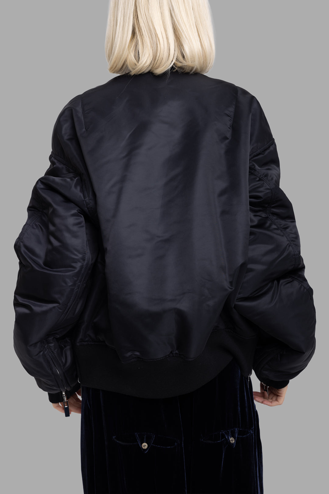 Comme des Garçons women's black bomber jacket, back view, smooth nylon shell with dropped shoulders.
