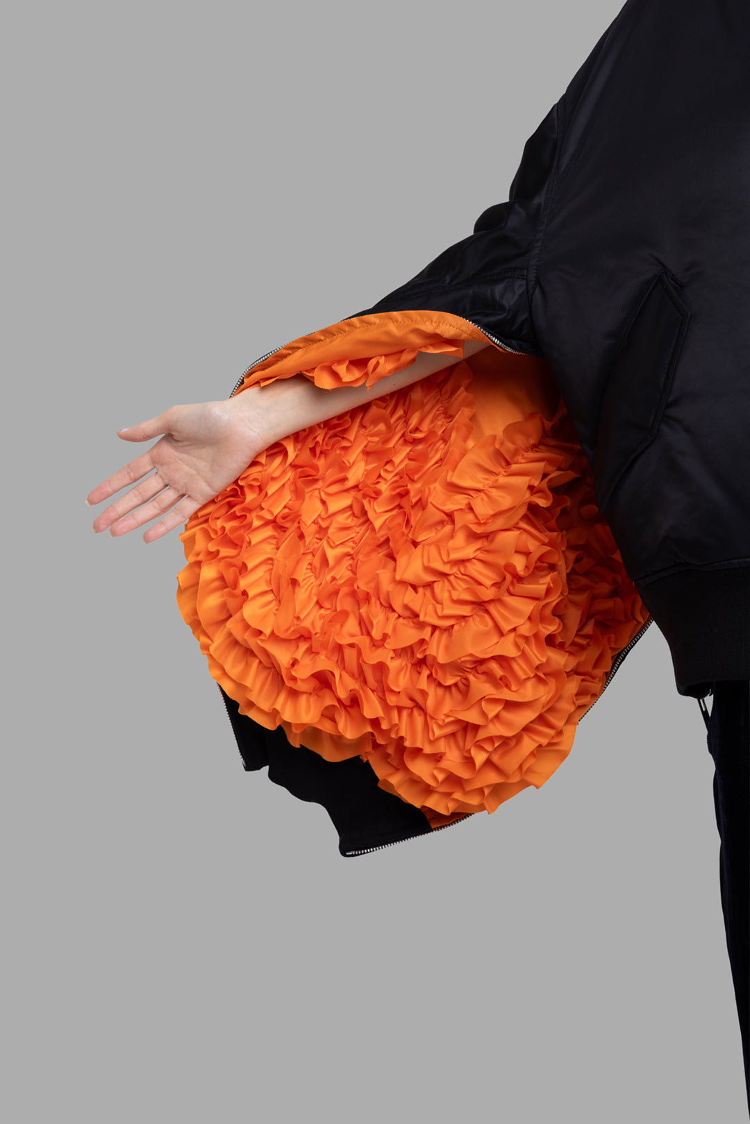 Comme des Garçons women's black bomber jacket, close-up of sleeve, vivid orange gathered ruffle lining.