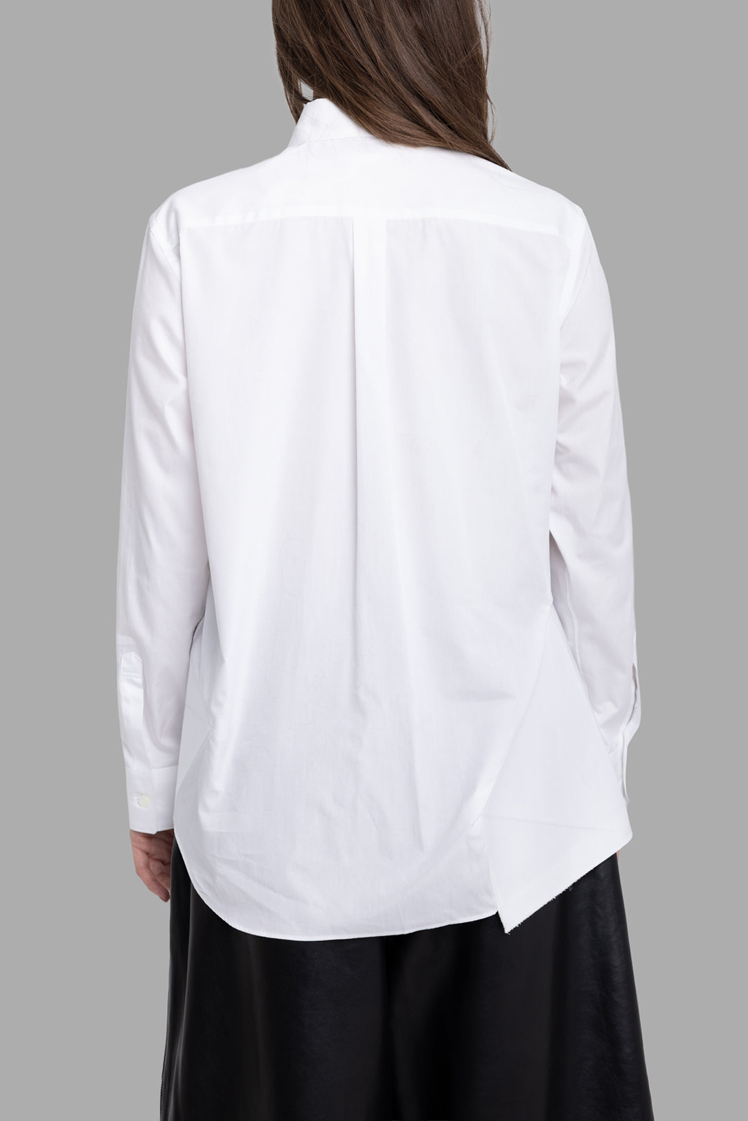 Comme des Garçons women's white ruffle bottom shirt, back view, clean yoke with soft pleat and asymmetric extended hem.