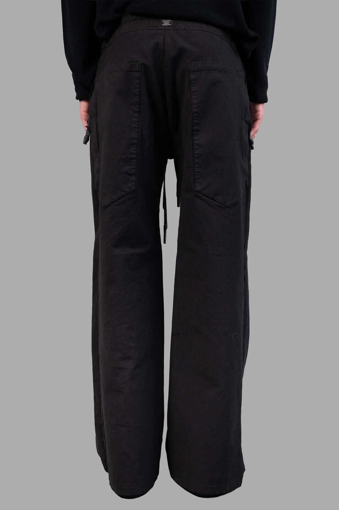 Isaac Sellam Drawstring Trousers in black, showcasing wide-legged silhouette and relaxed drawstring waist from the back view.
