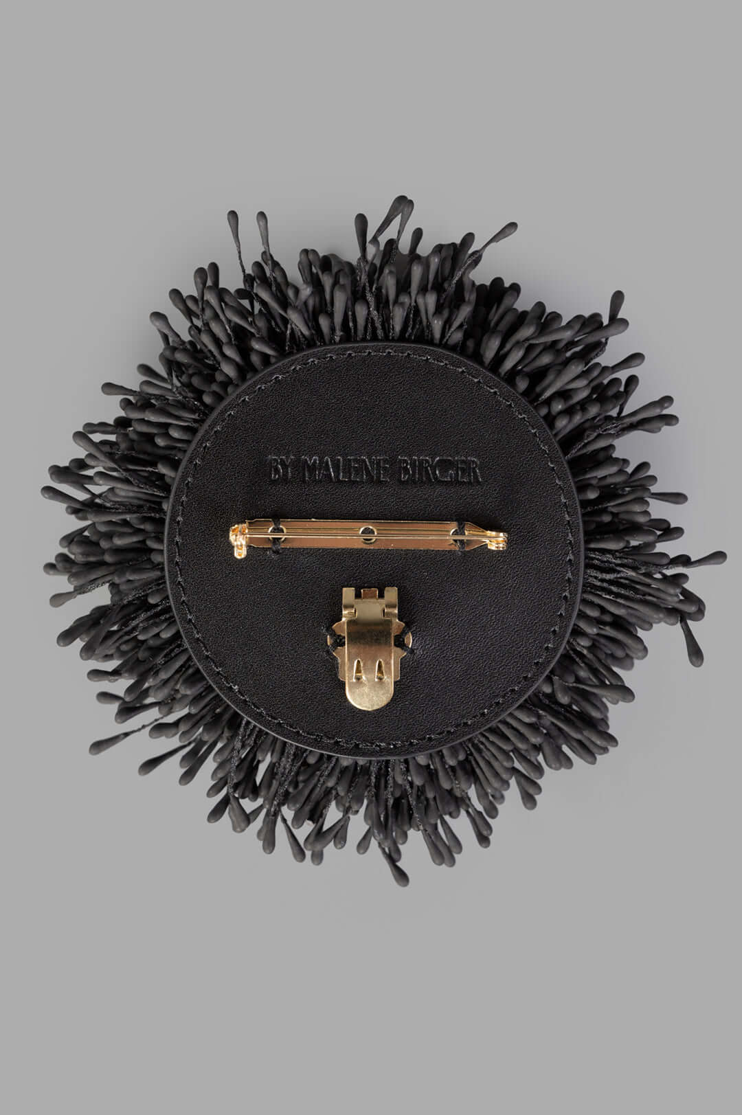By Malene Birger Henna Brooch in Black, featuring a textured, organic design with gold-tone fastener, viewed from above.
