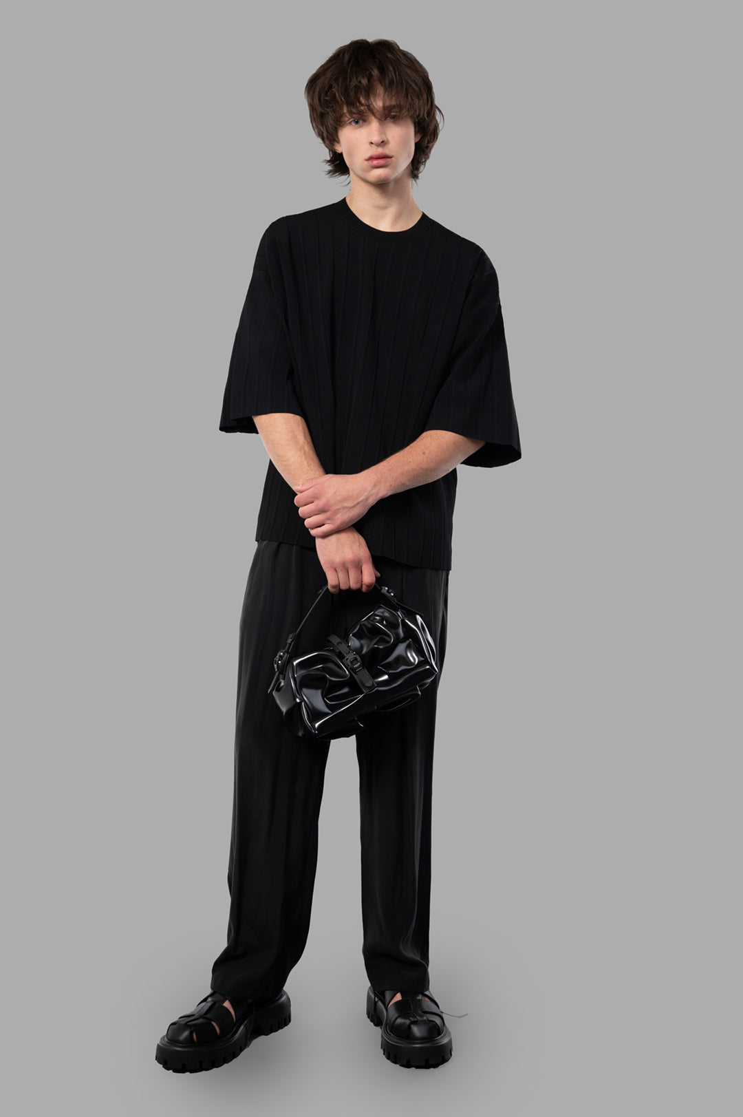 Attachment Pleated Trousers in black, on-model view, showcasing relaxed fit and sleek front pleats, with side pockets.