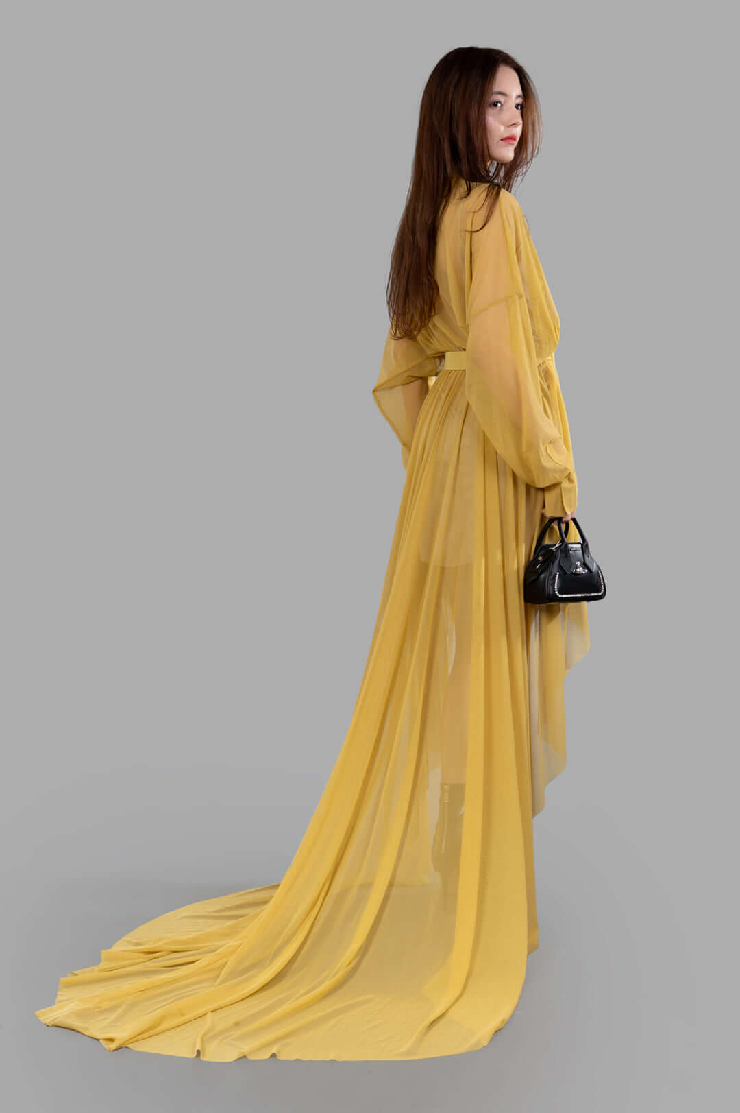 Norma Kamali Belted Shirt Gown, side view, model facing left, long yellow sheer fabric flowing on the floor.