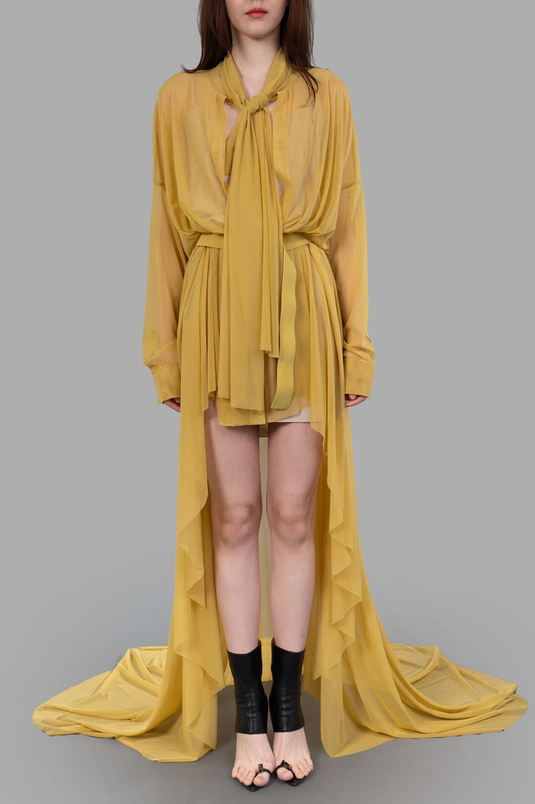Norma Kamali Belted Shirt Gown displayed on a model, featuring a flowing yellow design with a tied neckline and side ruffles.