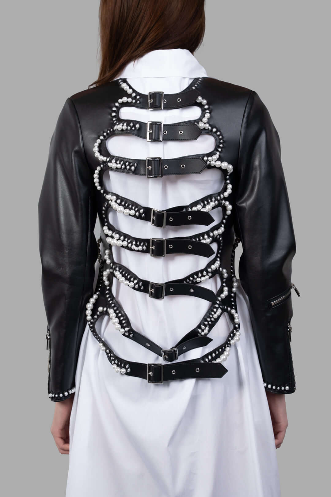 Noir Kei Ninomiya Pearl-Detailed Jacket showcasing back view with adjustable straps and pearl accents on sleek faux leather.