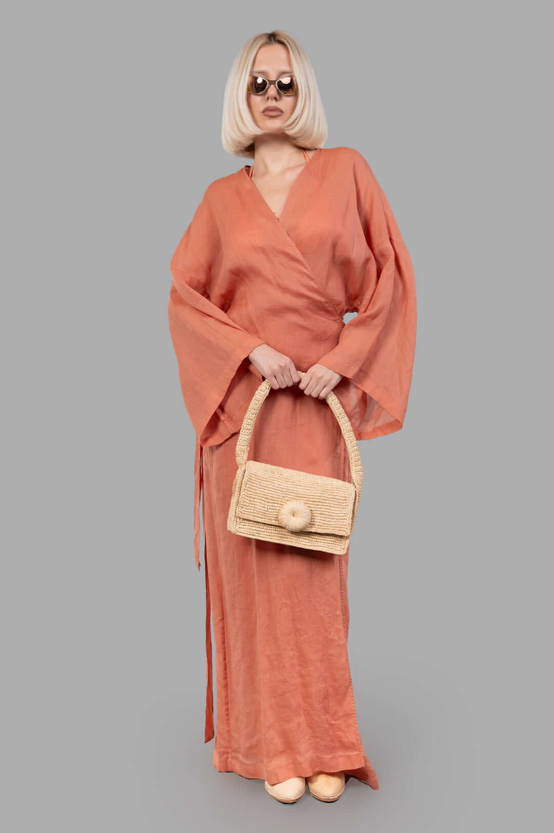 Fisico Pink Kimono with a Frame shown on model, front view. Coral color, maxi-length, sewn-in belt, paired with woven bag.
