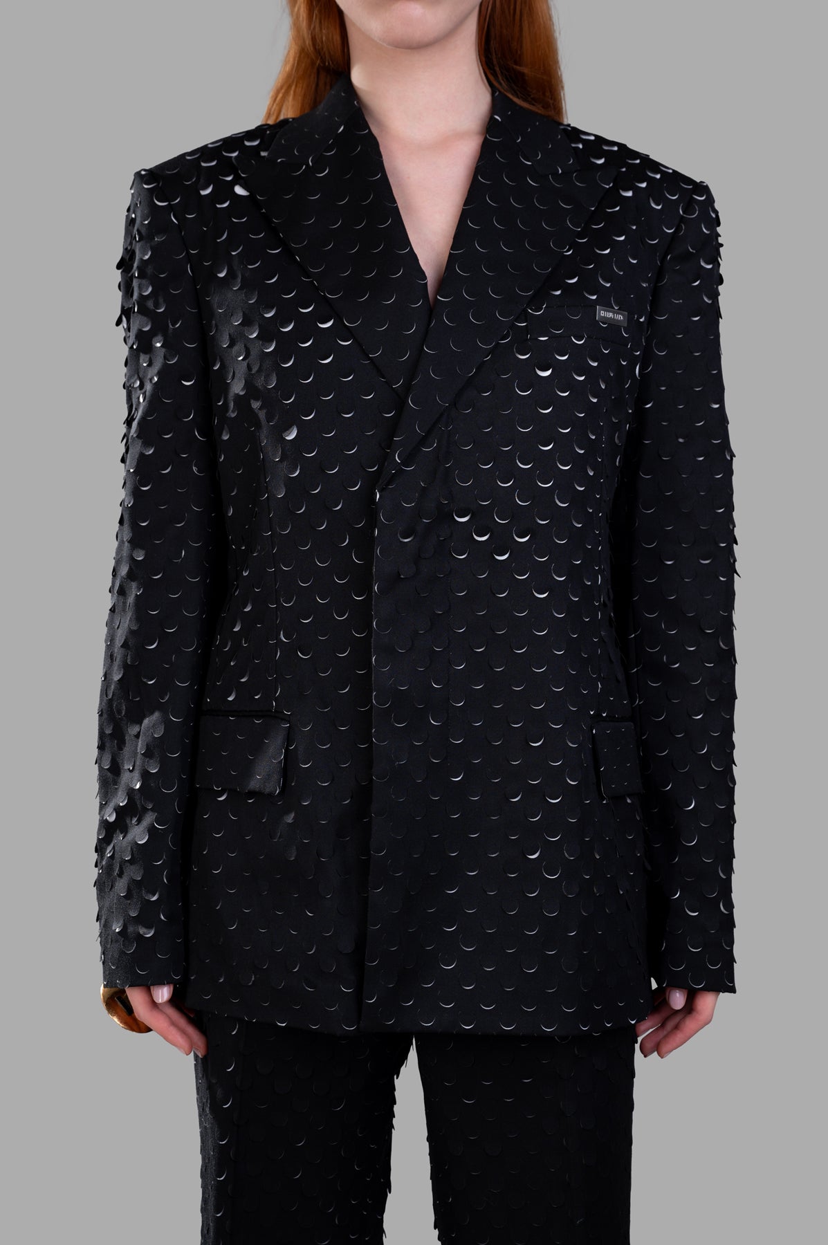 Helmut Lang Hole-Punched Car Blazer in black, featuring a textured finish, peak lapels, and flap pockets, styled on a model.