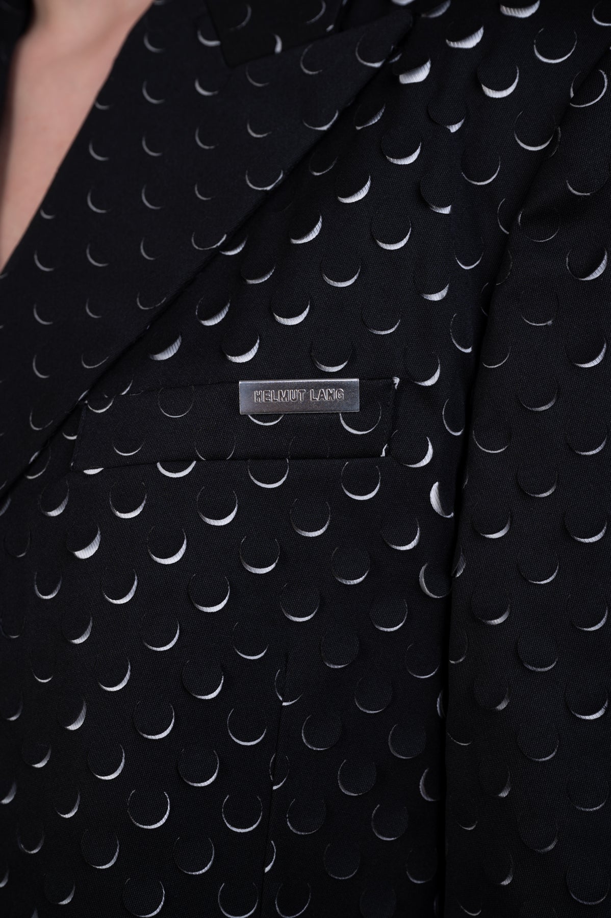 Helmut Lang Hole-Punched Car Blazer close-up showing laser-cut texture and logo detail on fabric in black.