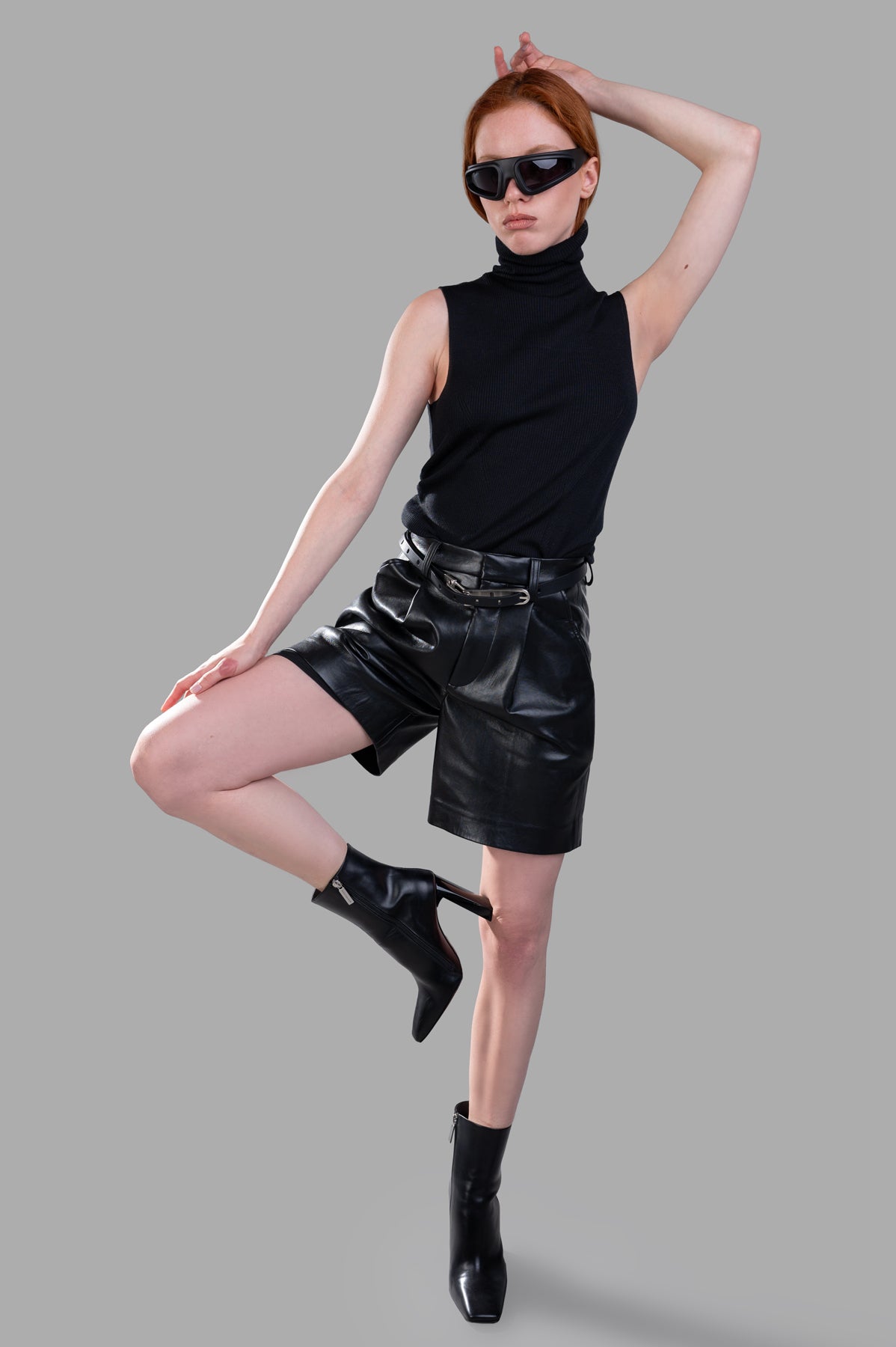 Gentry Portofino sleeveless sweater in black ribbed knit, turtleneck design, styled on-model with leather shorts.