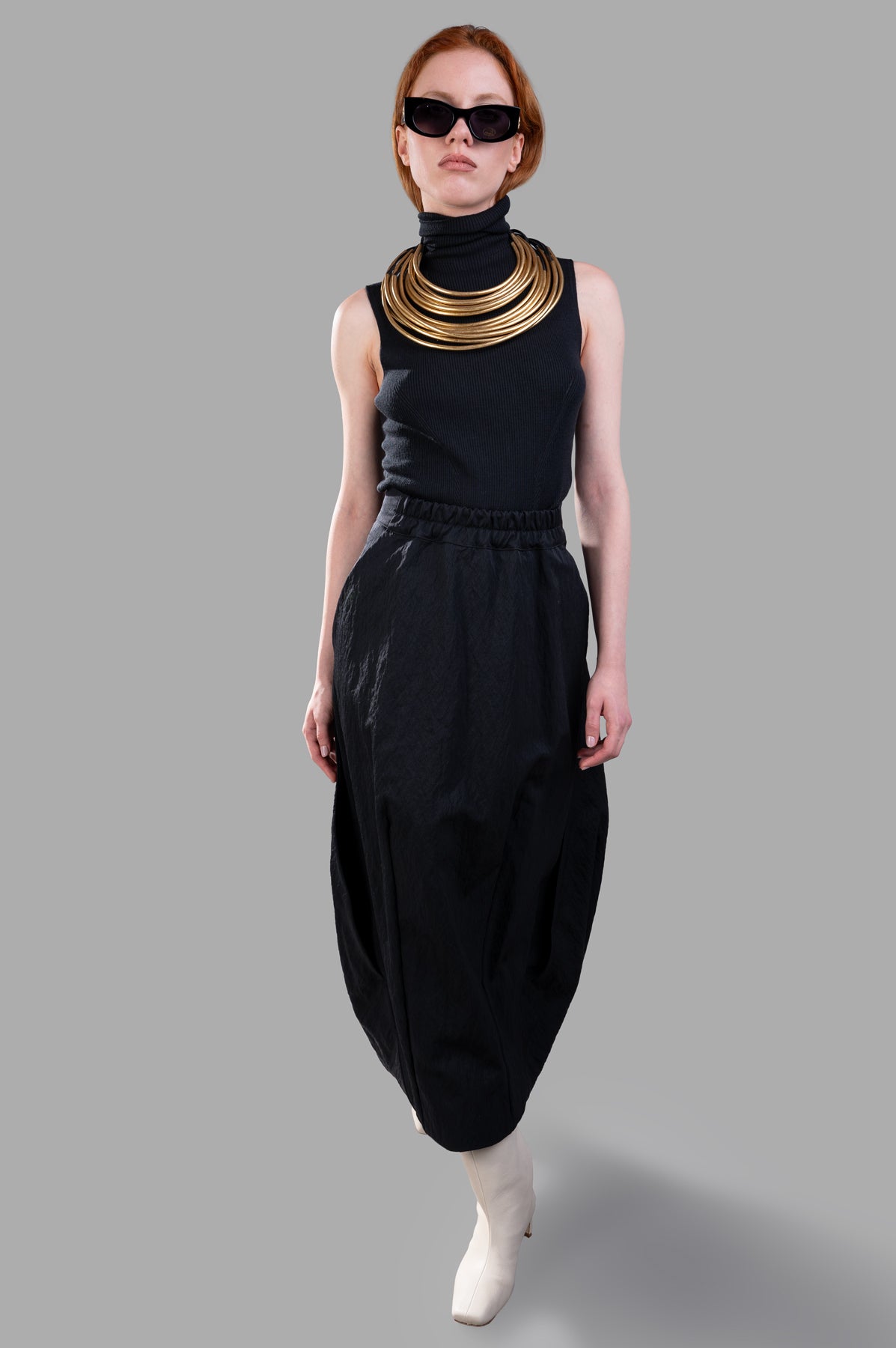 Gentry Portofino Balloon Skirt on model, front view. Model wears black top, statement necklace, sunglasses, and white boots.