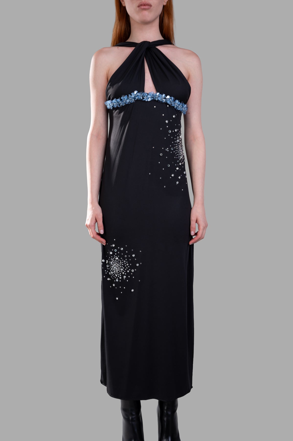 DES PHEMMES halterneck dress in black with a bedazzled waistband, showcasing a deep slit and elegant design on model.