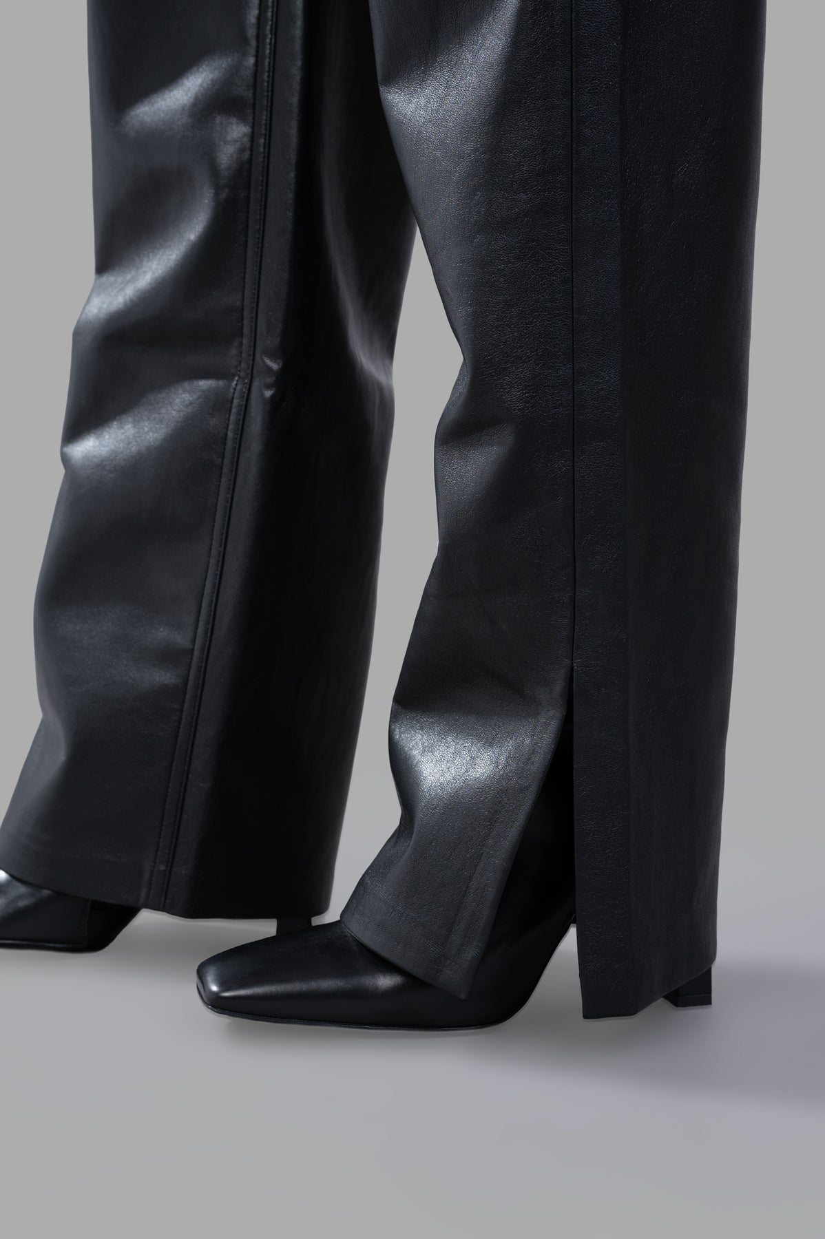 Anine Bing Roy Pants in black midweight regenerated leather with side slits, styled with sleek heels for a chic look.