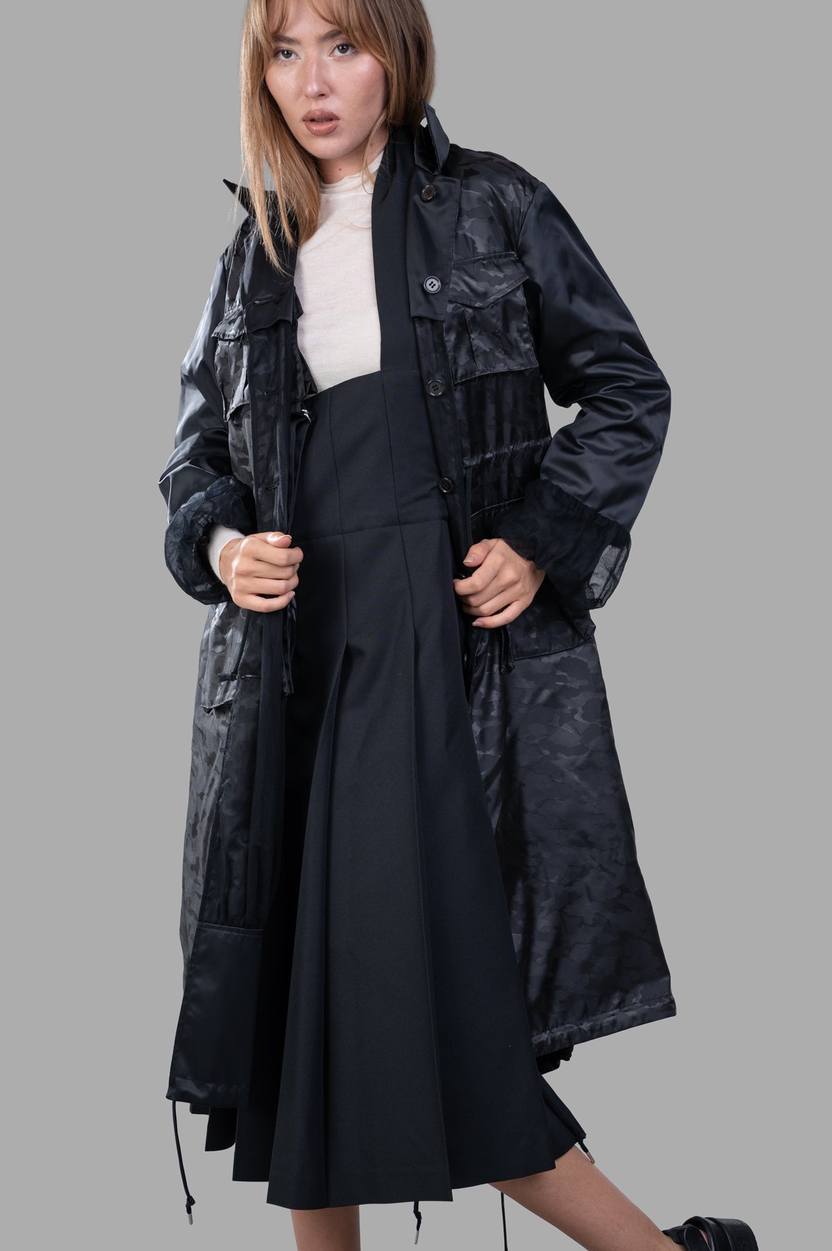 Noir Kei Ninomiya Reversible Trench Coat pictured on model from the side, highlighting the stylish ruffle cuffs and.