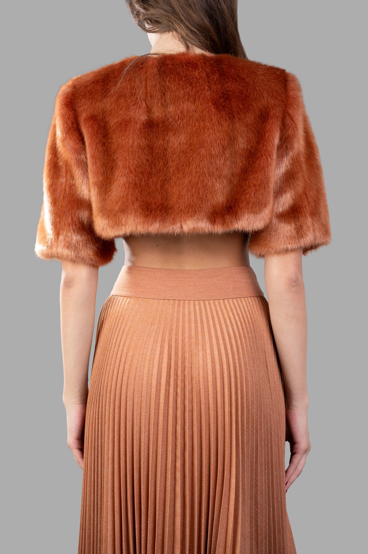 Alabama Muse Cropped Faux-Fur Jacket in Visone, showcasing luxurious texture and sustainable design, worn with a pleated skirt.